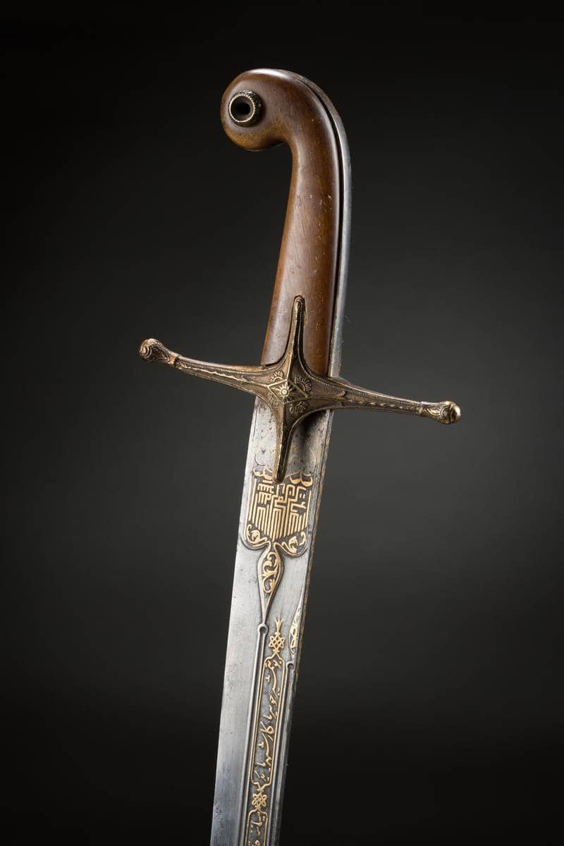 Gros plan sur les inscriptions en relief doré ornant la poignée d'un sabre ancien photographié pour la maison Ader
