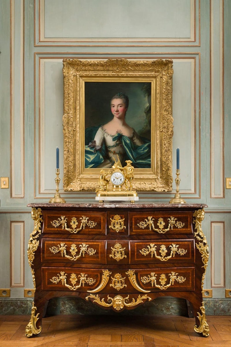 Commode ancienne surmontée d'une pendule et de bougeoirs en bronze doré dans une galerie à Versailles