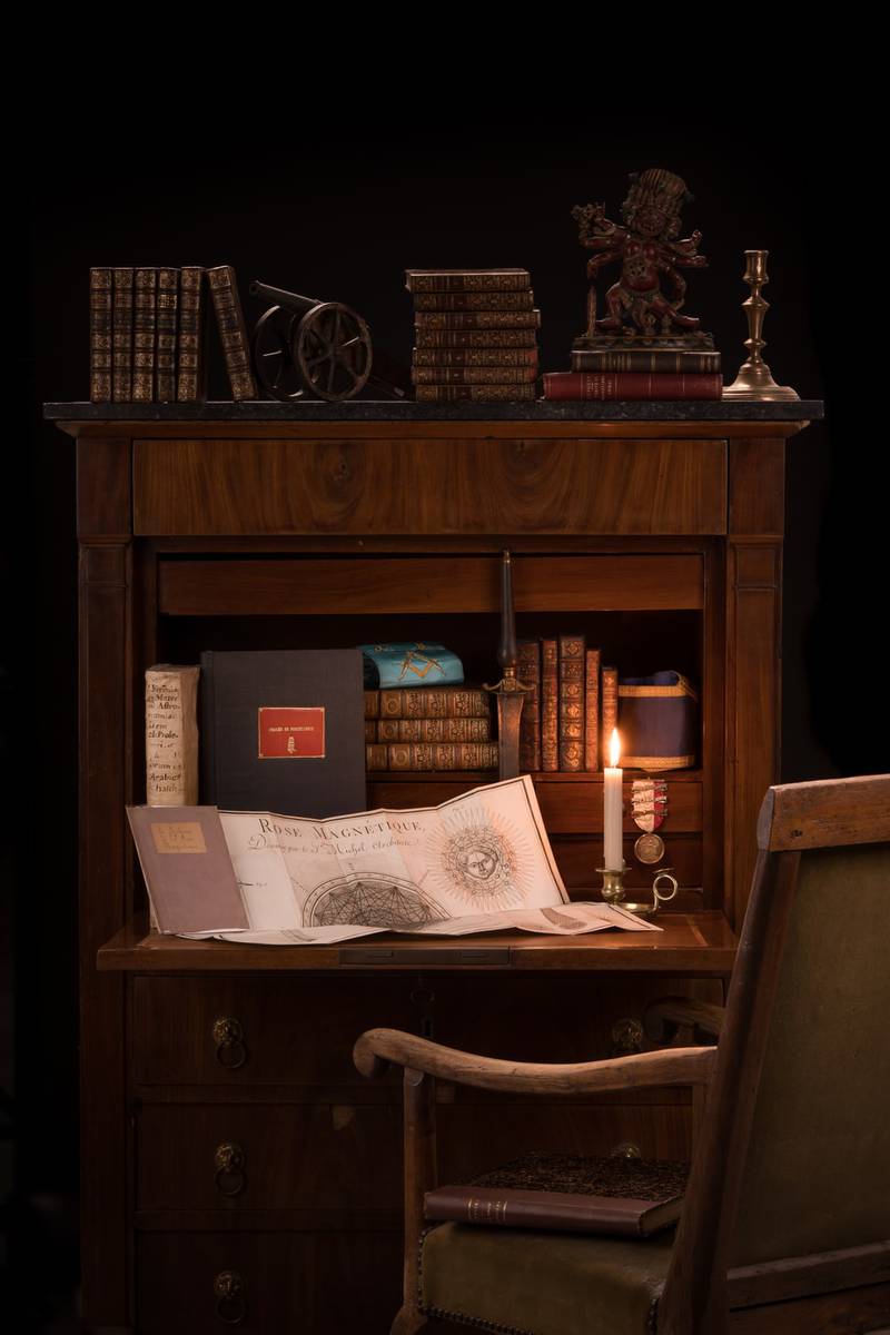 Secrétaire ancien avec abattant ouvert, livres et objets d'art dans une atmosphère chaleureuse éclairée à la bougie