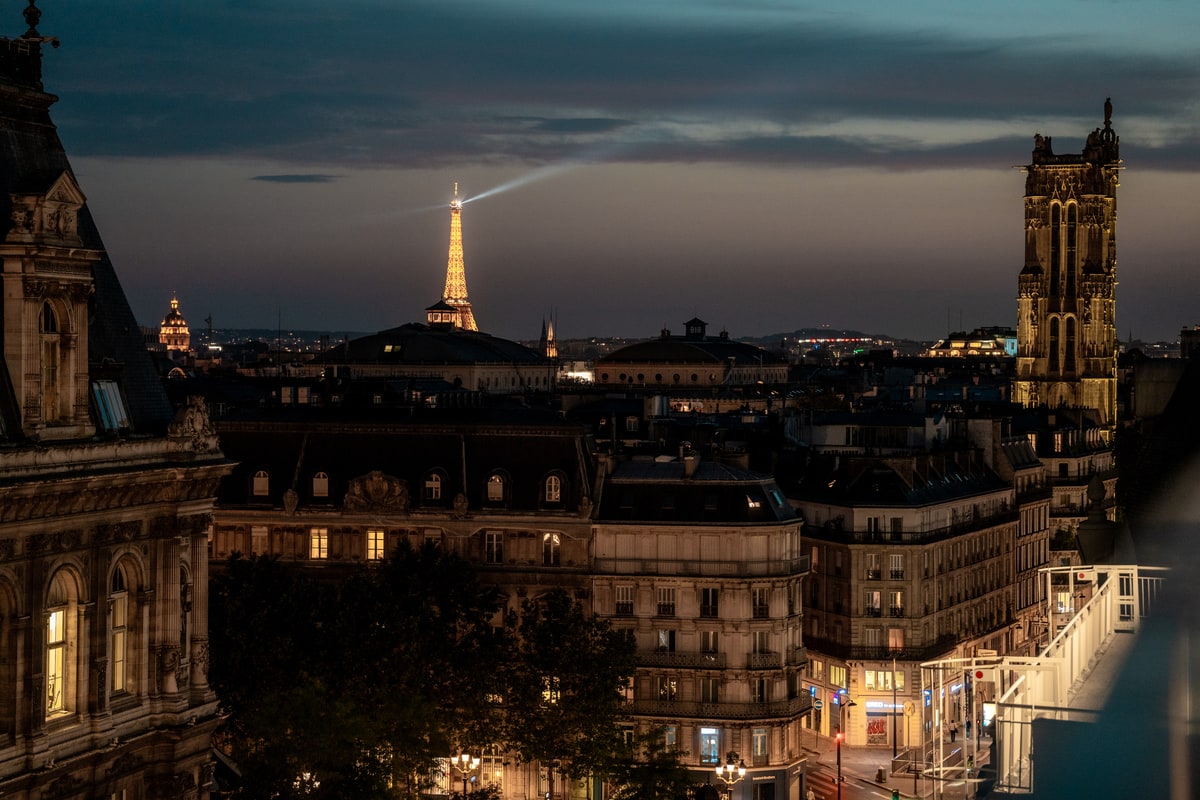 Tour Eiffel illuminée de nuit avec son faisceau lumineux traversant le ciel, vue depuis Terraza Mikuna au BHV Le Marais.